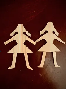 Two figures cut freehand from lined notebook paper, standing side by side on a dark wooden table